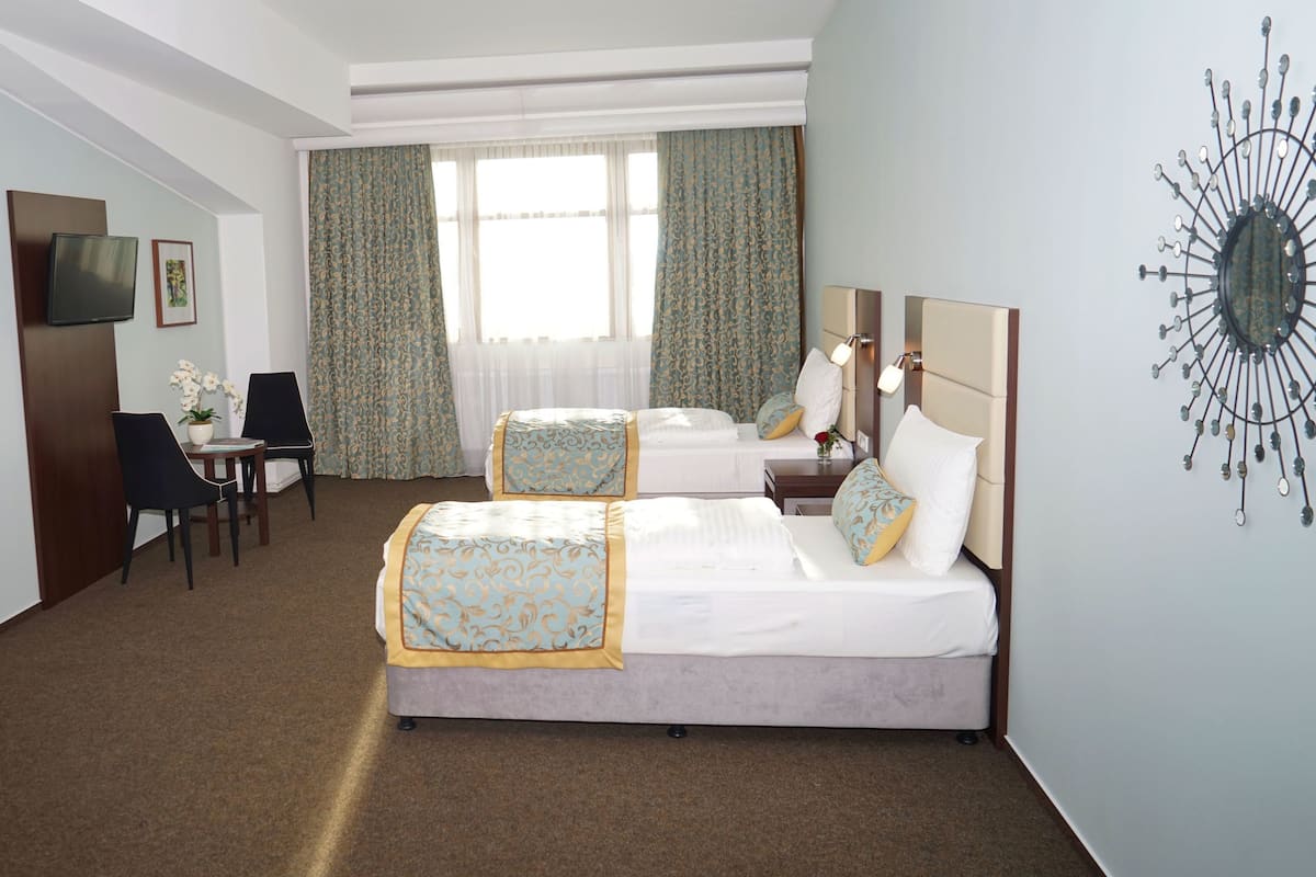 Ein Hotelzimmer mit zwei Betten, einem Schreibtisch, einem Sessel, einem Fernseher und einer Wanddekoration.