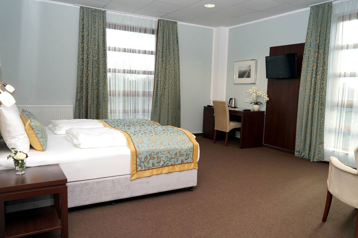 Ein Hotelzimmer mit Bett, Schreibtisch, Stuhl, Fernseher und einem fenster mit Vorhängen.