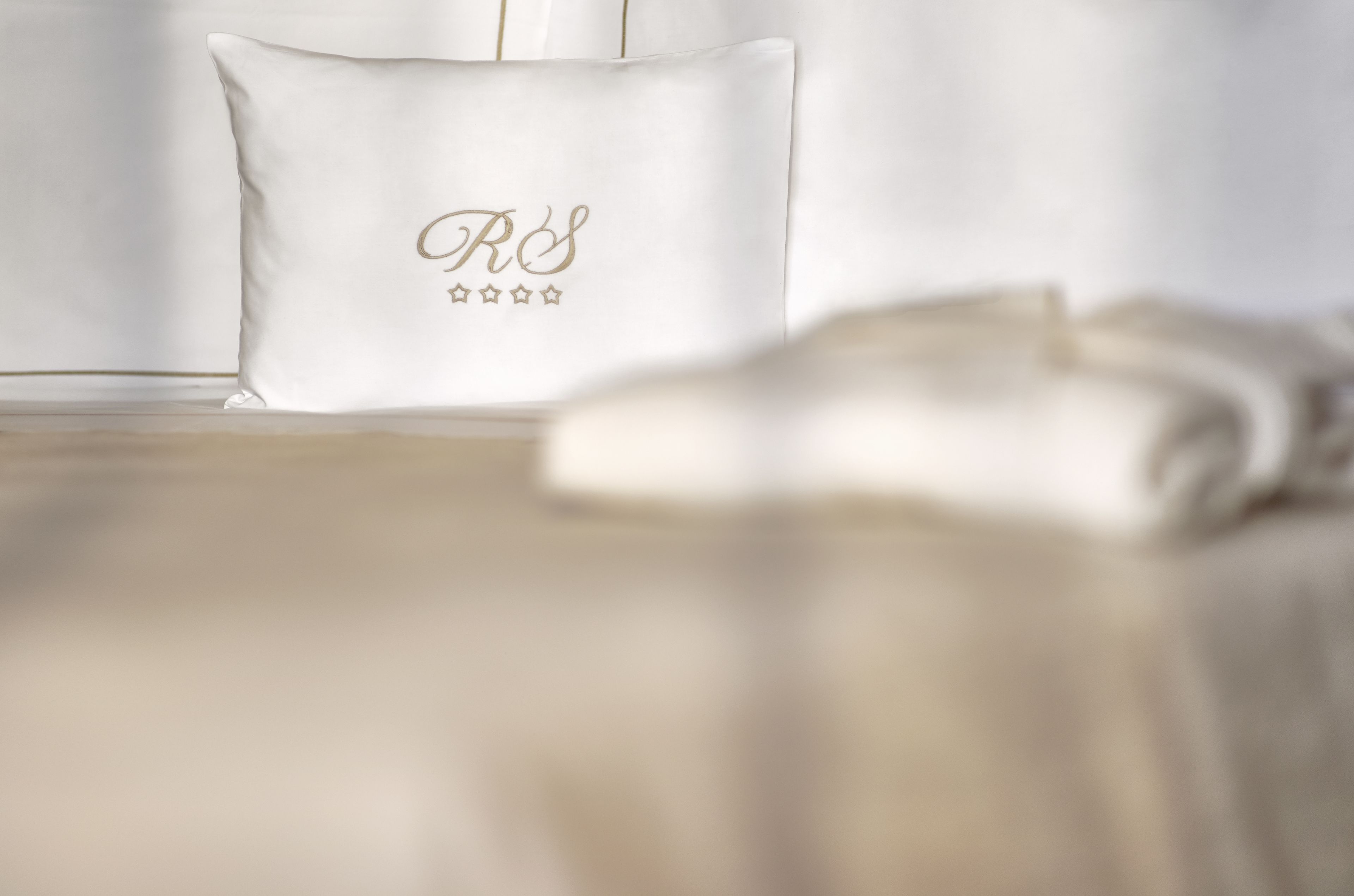 Un lit avec un oreiller blanc orné d’un monogramme et de cinq étoiles.