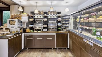 Mostrador de panadería con diversas opciones de productos horneados, una máquina de café y una vitrina con pastelería.