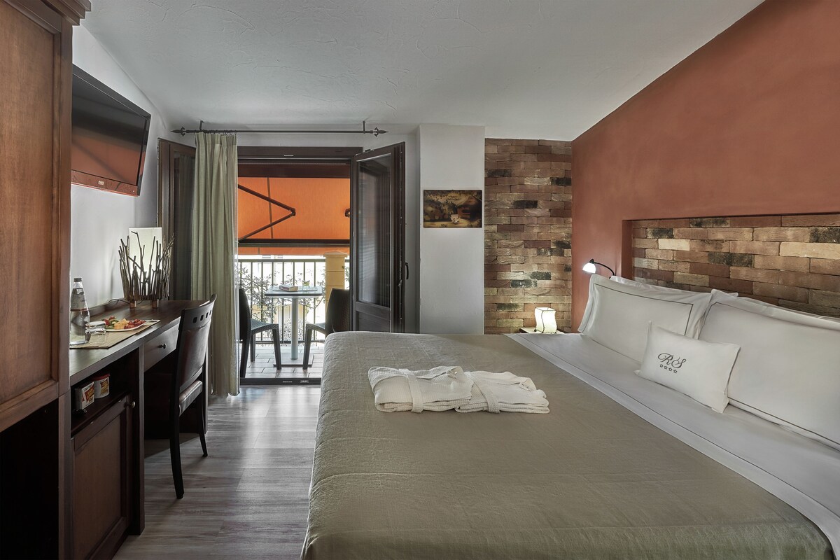 A hotel room with a bed, a desk, a chair, a table with chairs, and a view of the outside.