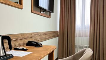 A hotel room with a wooden desk, a television mounted on the wall, a telephone, and a chair.