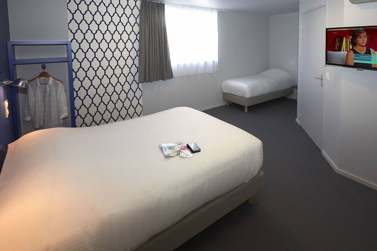 A hotel room with a large bed, a smaller bed, a TV, and a wardrobe.