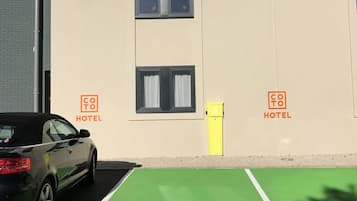 Un hotel con un coche estacionado en un espacio reservado, un carril bici verde y un contenedor amarillo.