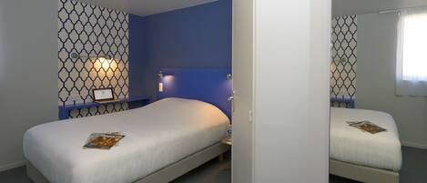 A bedroom with two beds, a nightstand, a wall-mounted lamp, and a security camera.