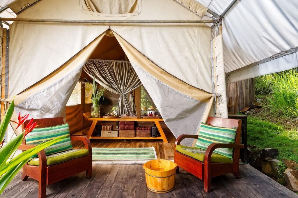A tent with a wooden deck, two wooden chairs with cushions, a small table, and a wooden bucket.