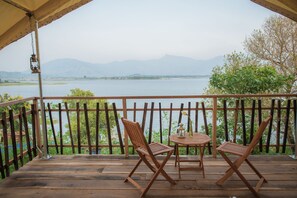 A wooden deck with two folding chairs and a small table, overlooking a lake with mountains in the background. - Lak Tented Camp (Lak)