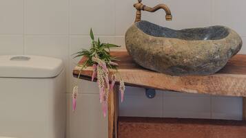 Un baño con lavamanos de piedra, estante de madera y un inodoro.