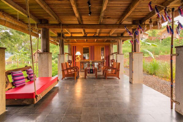A wooden covered area with a red bench, a table with chairs, and a view of greenery outside. - Lak Tented Camp (Lak)