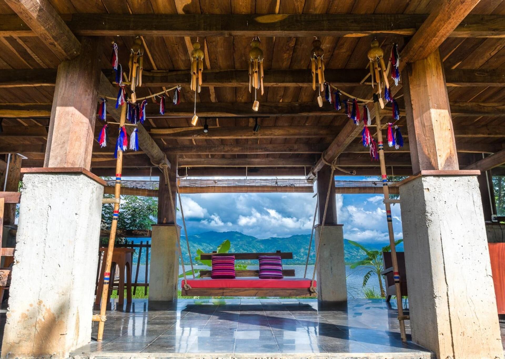 A wooden pavilion with a bench and hanging wind chimes, overlooking a mountainous landscape.