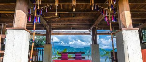 A wooden pavilion with a bench and hanging wind chimes, overlooking a mountainous landscape.