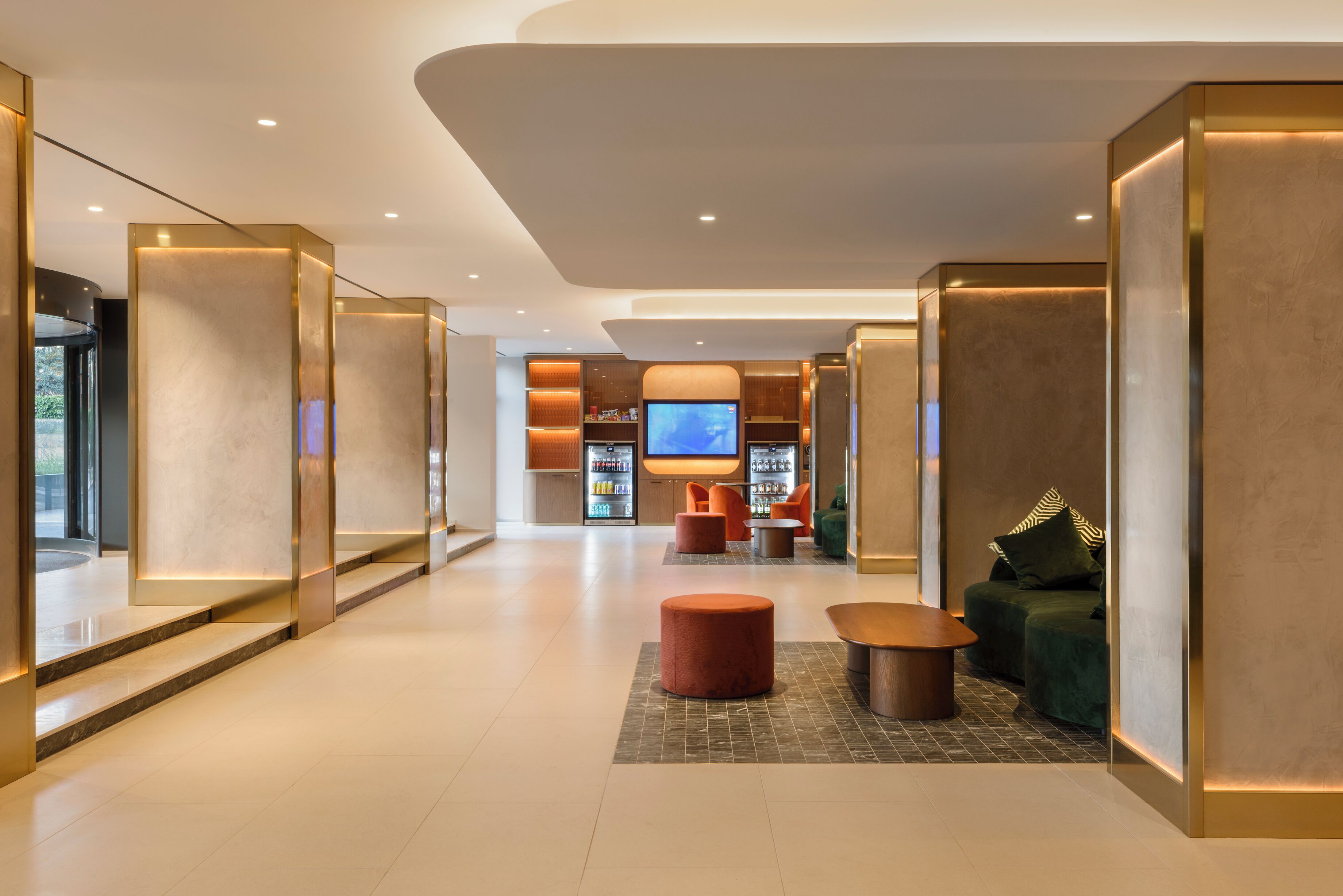 A modern lobby with a TV, seating area, and vending machines.