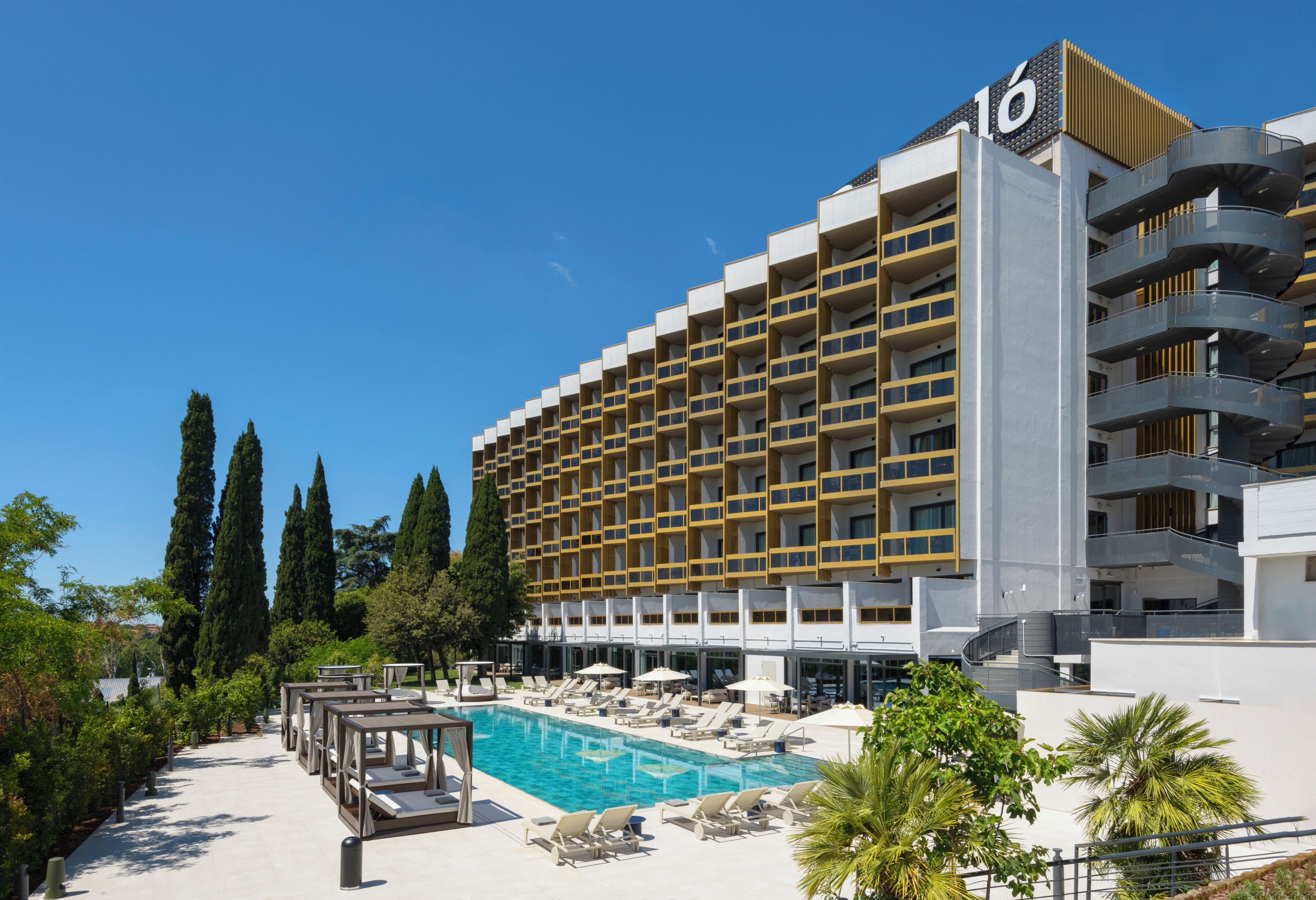 A hotel with a pool, multiple balconies, and a clear blue sky.