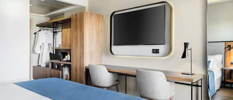 A modern hotel room with a large bed, a desk with two chairs, a wardrobe, a mirror, and a TV.