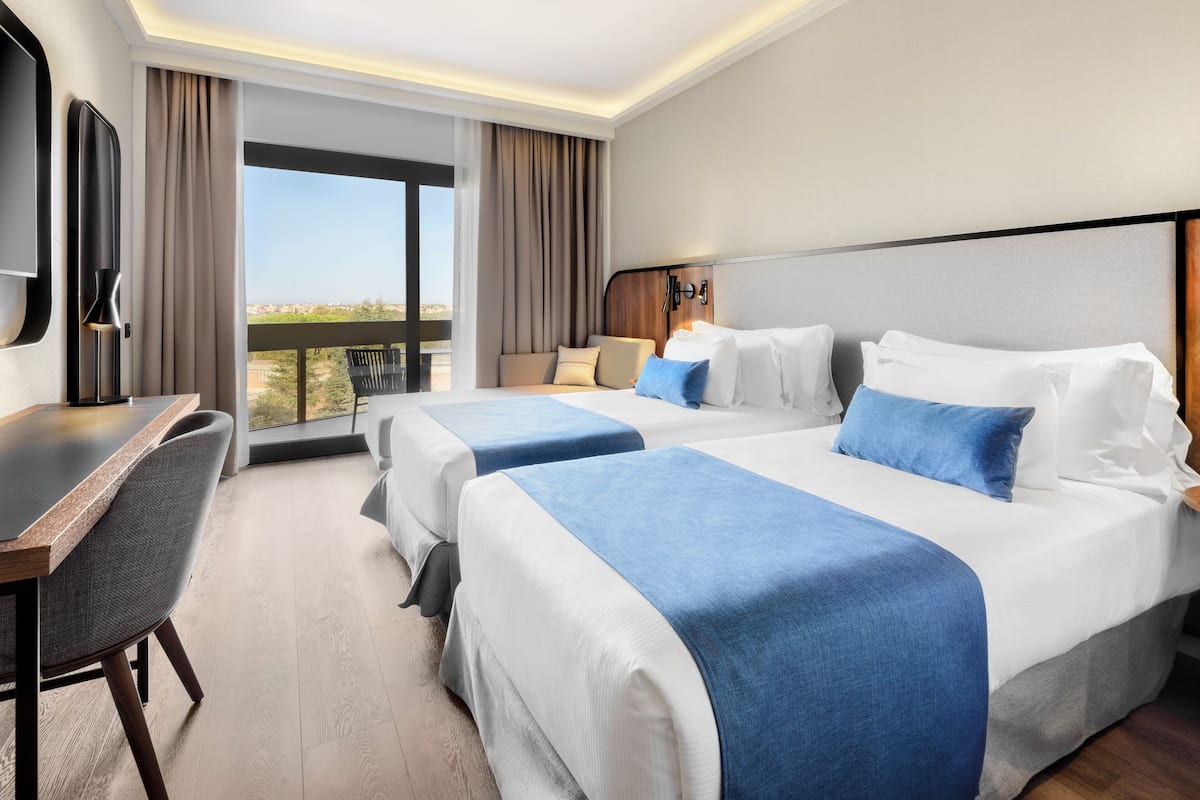 A hotel room with two beds, a desk, and a large window with a view.