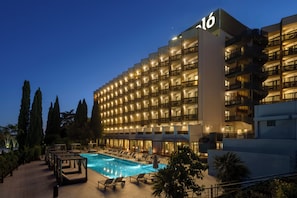 A hotel with a swimming pool, multiple balconies, and a well-lit facade.