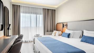 Una camera d'albergo con un letto grande, una scrivania con sedie, una TV e una finestra con tende.