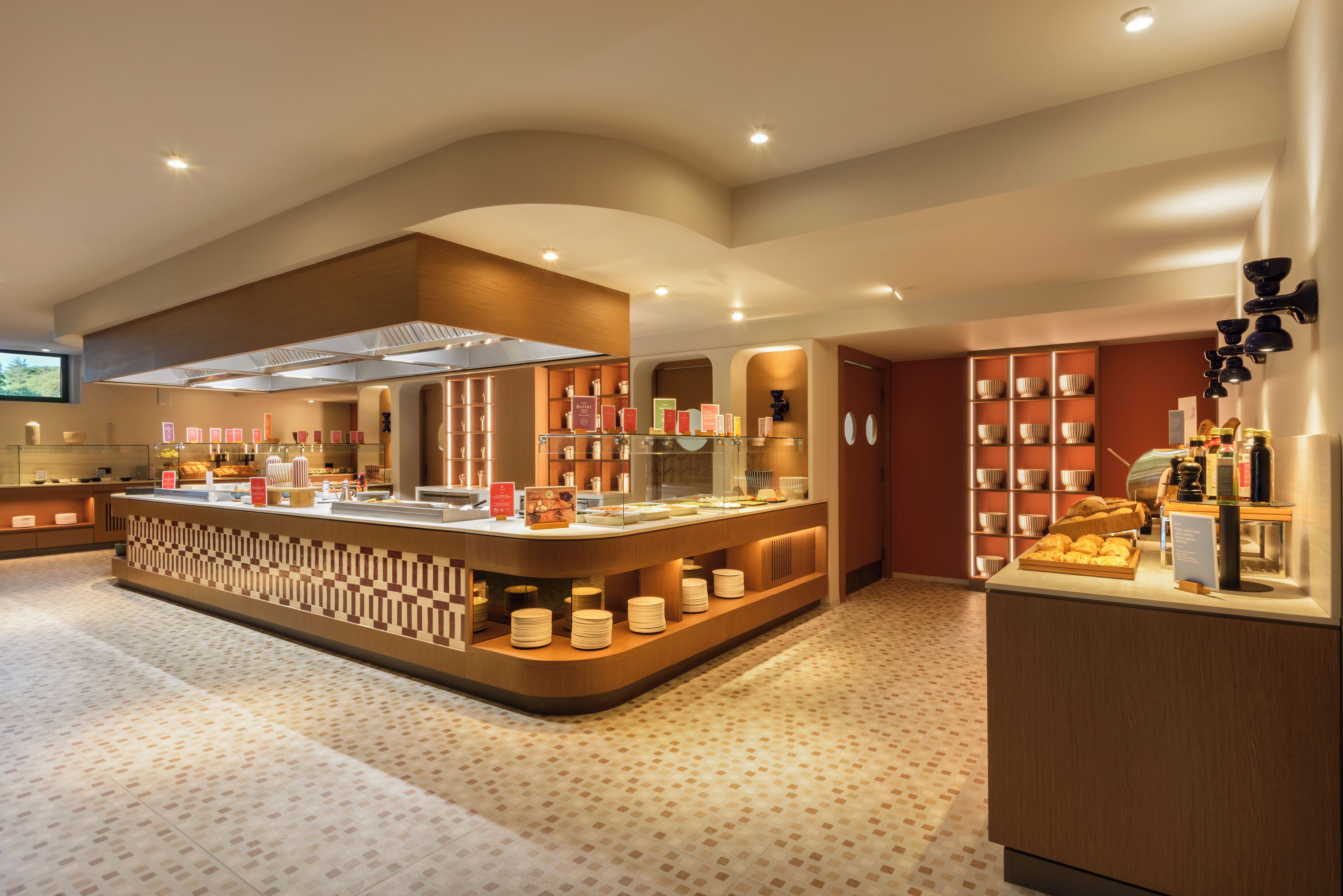 Un hall d’hôtel moderne doté d’un espace de réception central, d’un grand comptoir et d’un coin salon avec un sol à motifs.