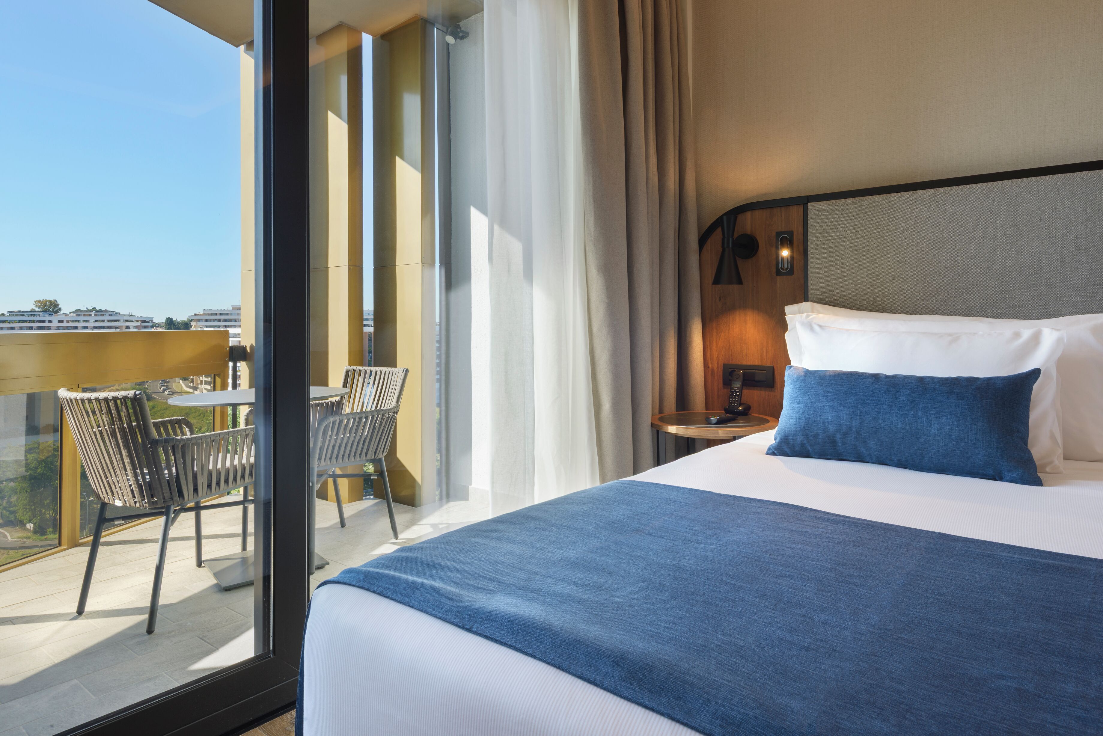 Een hotelkamer met een groot bed, een balkon met stoelen en uitzicht op de stad.