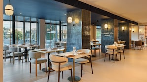A modern restaurant interior with tables, chairs, and large windows.
