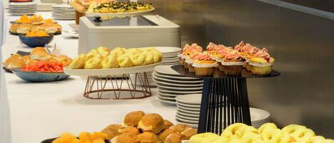 A buffet with various food items, including pastries, fruits, and sandwiches.