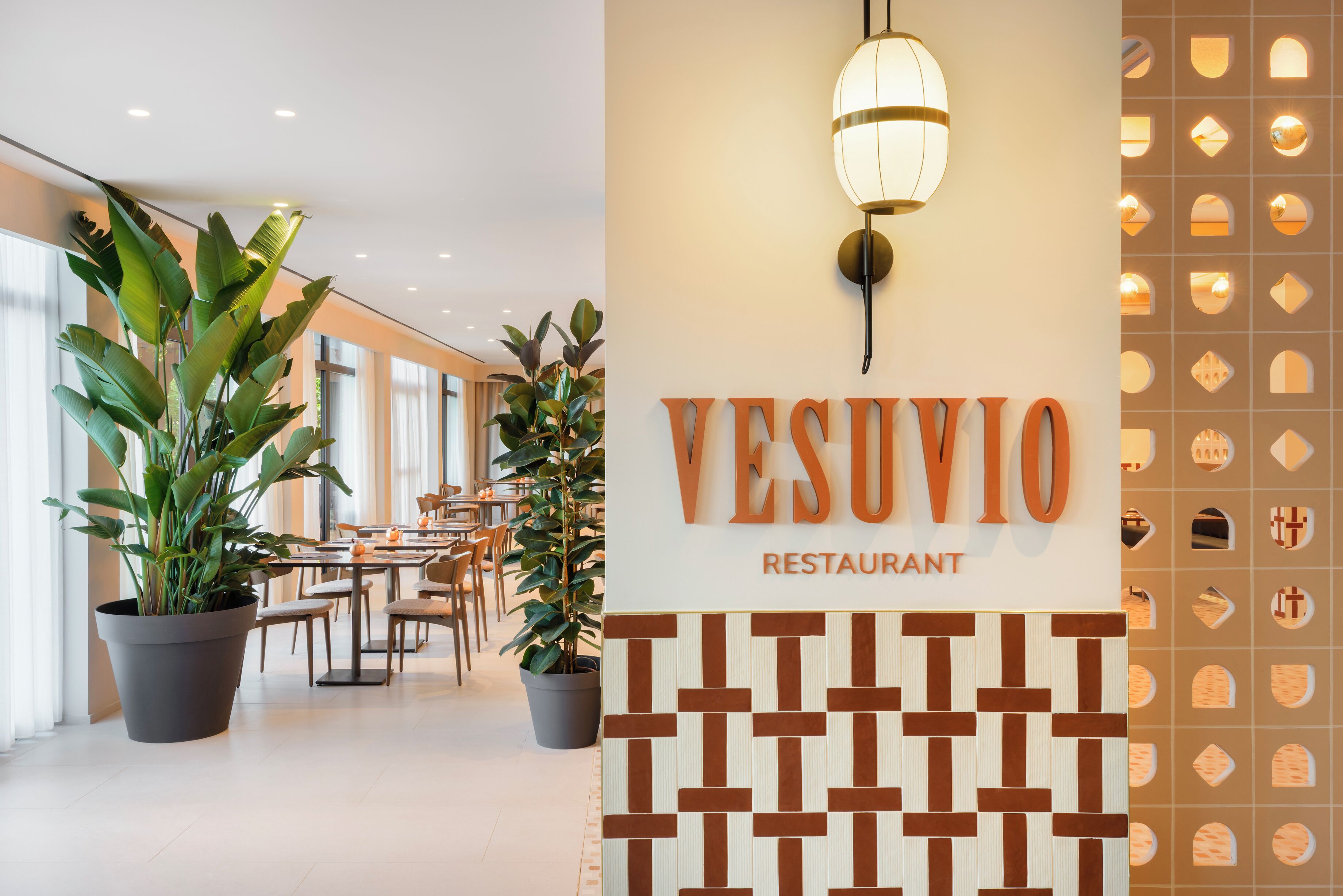 Interior de restaurant amb plantes en testos, taules, caires i un rètol fixat a la paret.