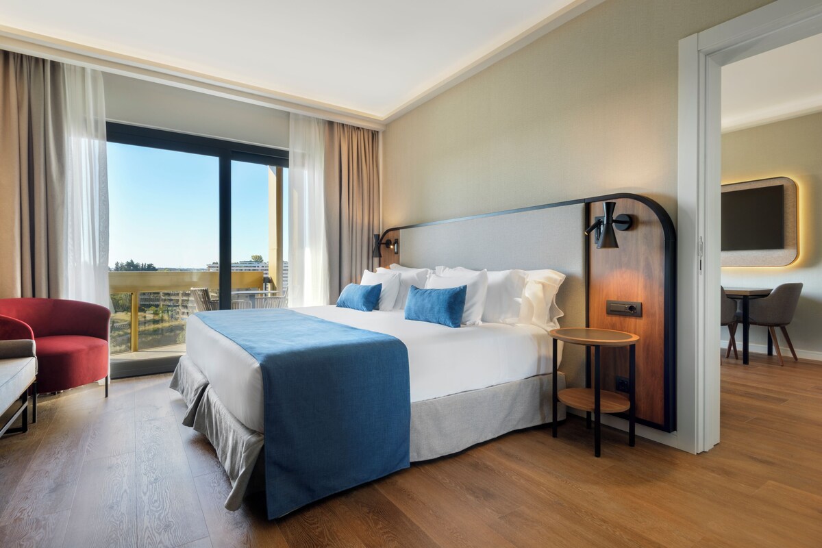 A hotel room with a large bed, a desk, a chair, and a view of the city.