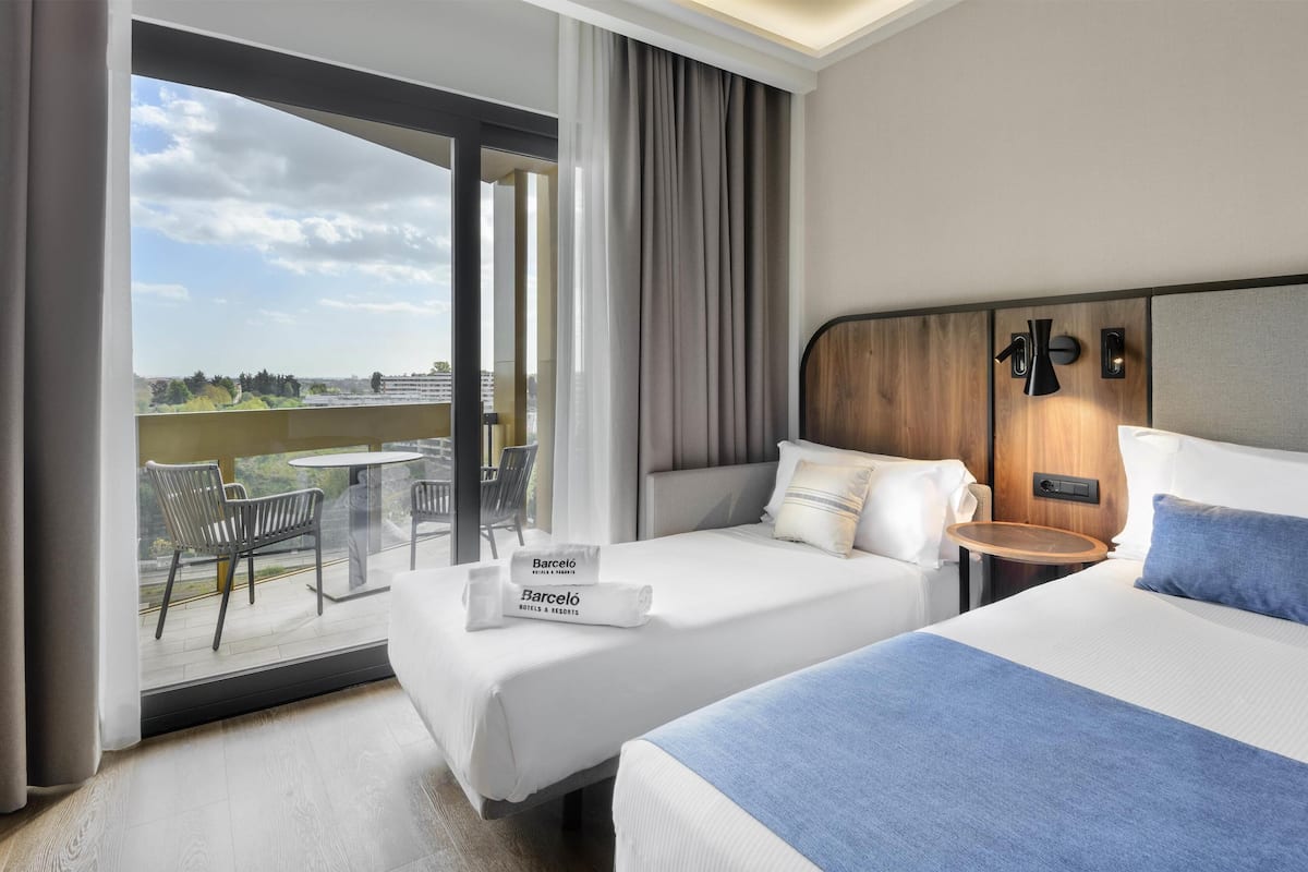 A hotel room with two beds, a balcony with a table and chairs, and a view of the cityscape.