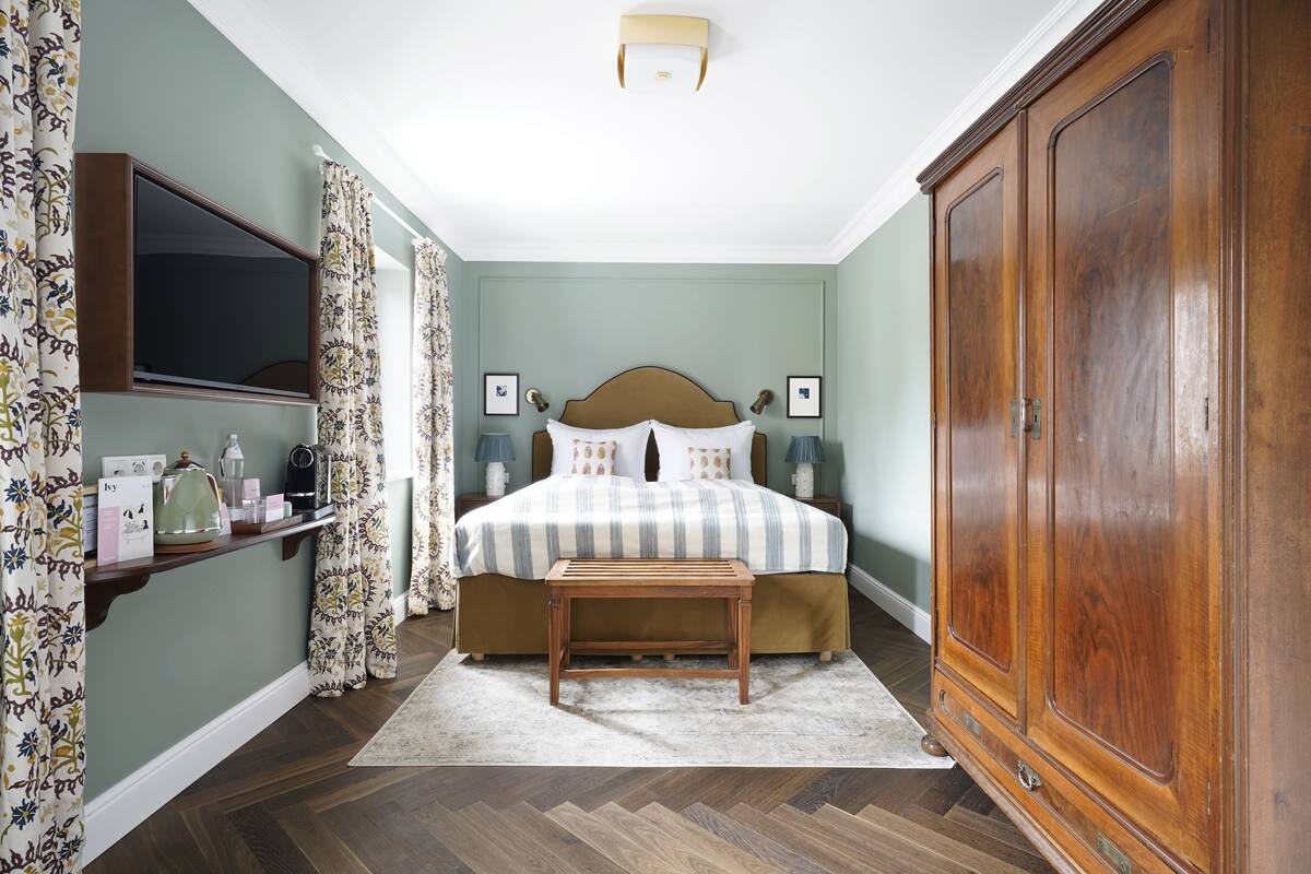 Quarto com cama, mesas de cabeceira, guarda-roupa de madeira, espelho e cortina estampada.