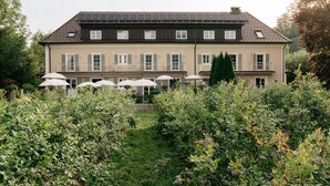 A two-story building with a balcony on the upper floor, surrounded by lush greenery and a garden with white umbrellas. - Numa Salzburg Ivy (Anif)