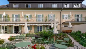 A two-story building with a balcony, outdoor seating area with tables and chairs, and umbrellas. - Numa Salzburg Ivy (Anif)