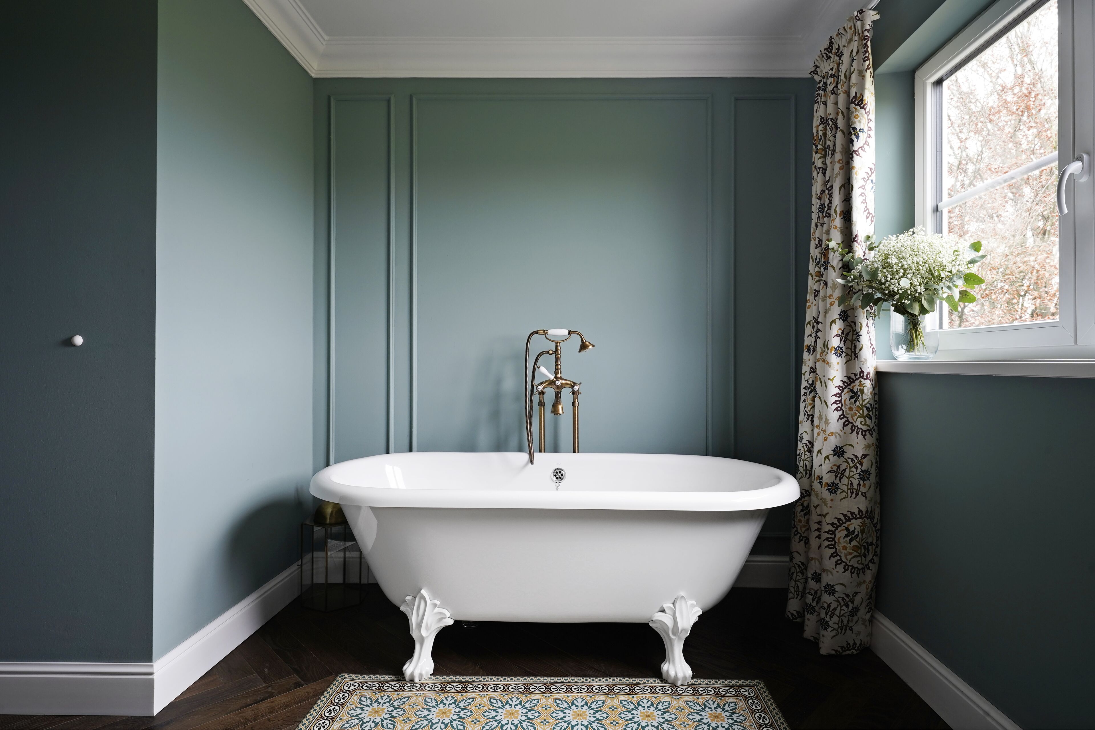A bathroom with a freestanding clawfoot bathtub, a white sink, and a window with a floral curtain.
