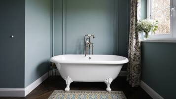 A bathroom with a freestanding clawfoot bathtub, a white sink, and a window with a floral curtain.