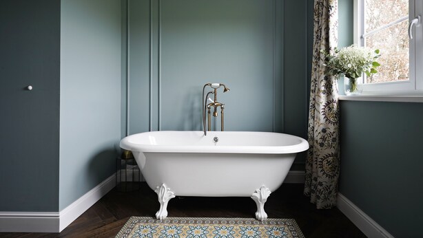 A bathroom with a freestanding clawfoot bathtub, a white sink, and a window with a floral curtain. - Numa Salzburg Ivy (Anif)