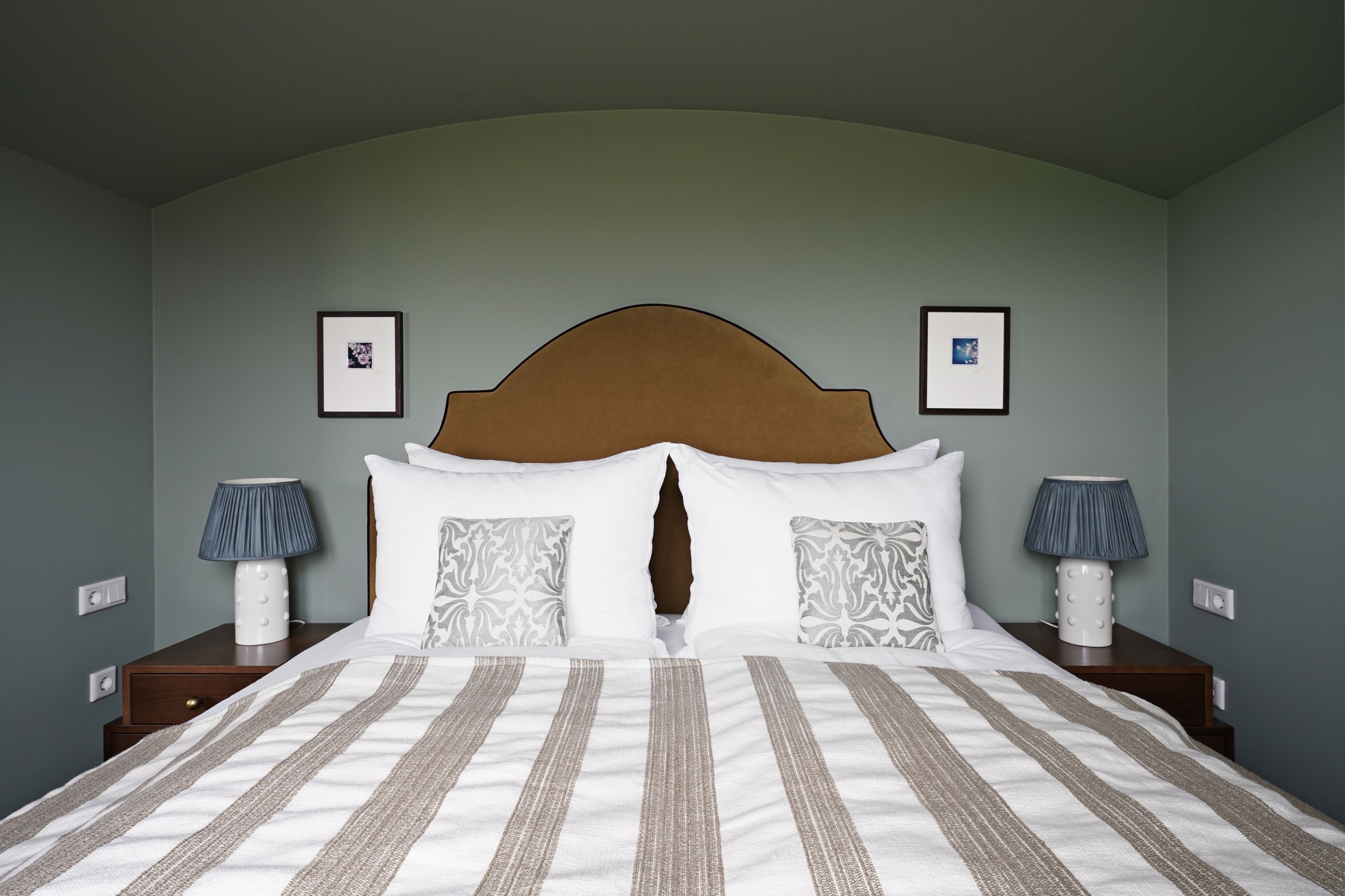 Un letto rifatto con cura, una coperta a righe, due lampade ai lati e una testiera con un decoro.
