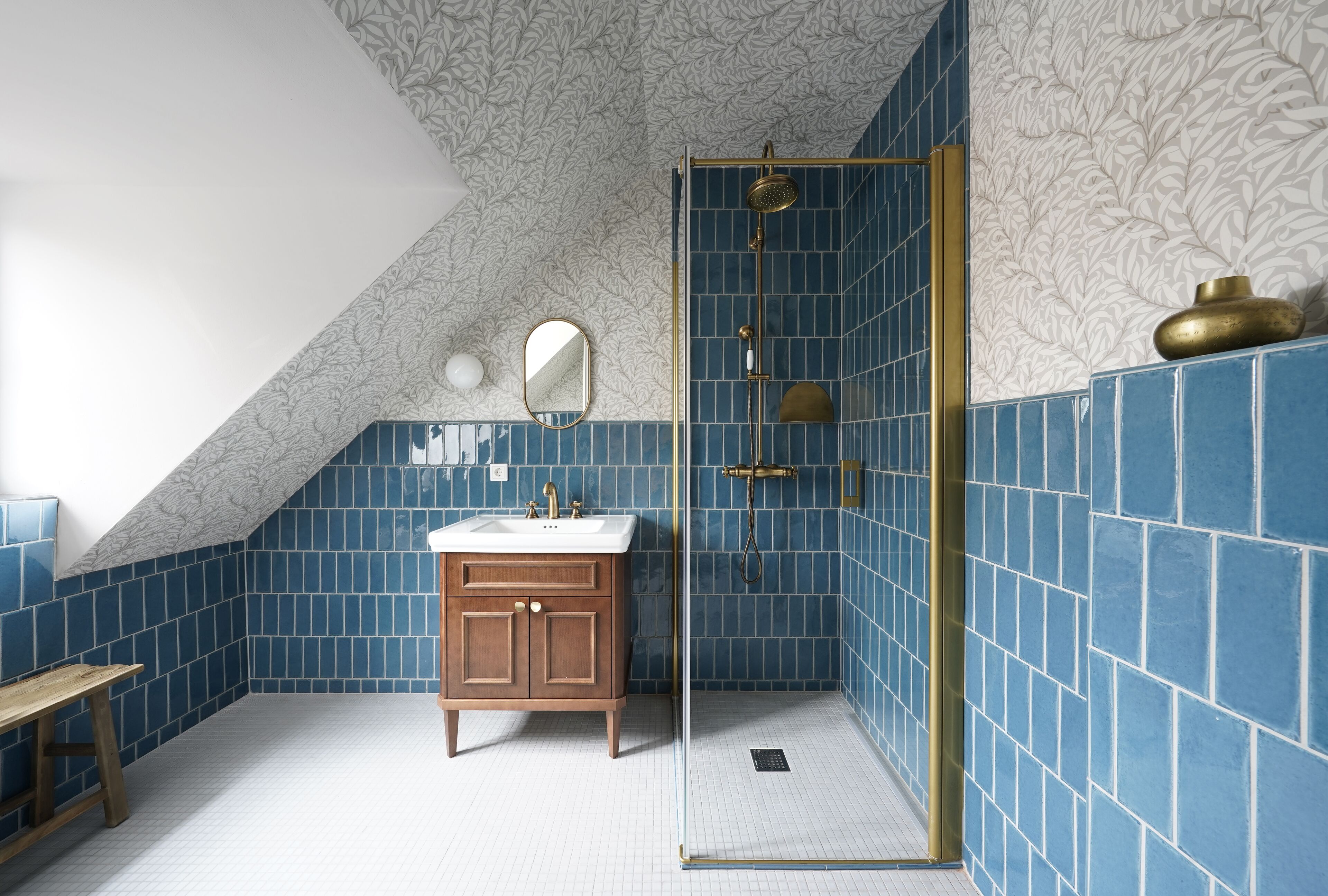 Ein Badezimmer mit blauen Fliesen, einem Holzkosmetikschrank, einem Spiegel und einer Dusche mit goldener Umrandung.