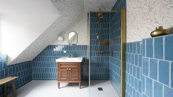 A bathroom with blue tiles, a wooden vanity, a mirror, and a shower with a gold frame.