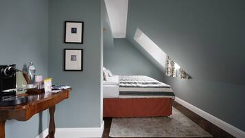 A bedroom with a sloped ceiling, a bed with a striped bedspread, a desk with a computer, and framed pictures on the wall.