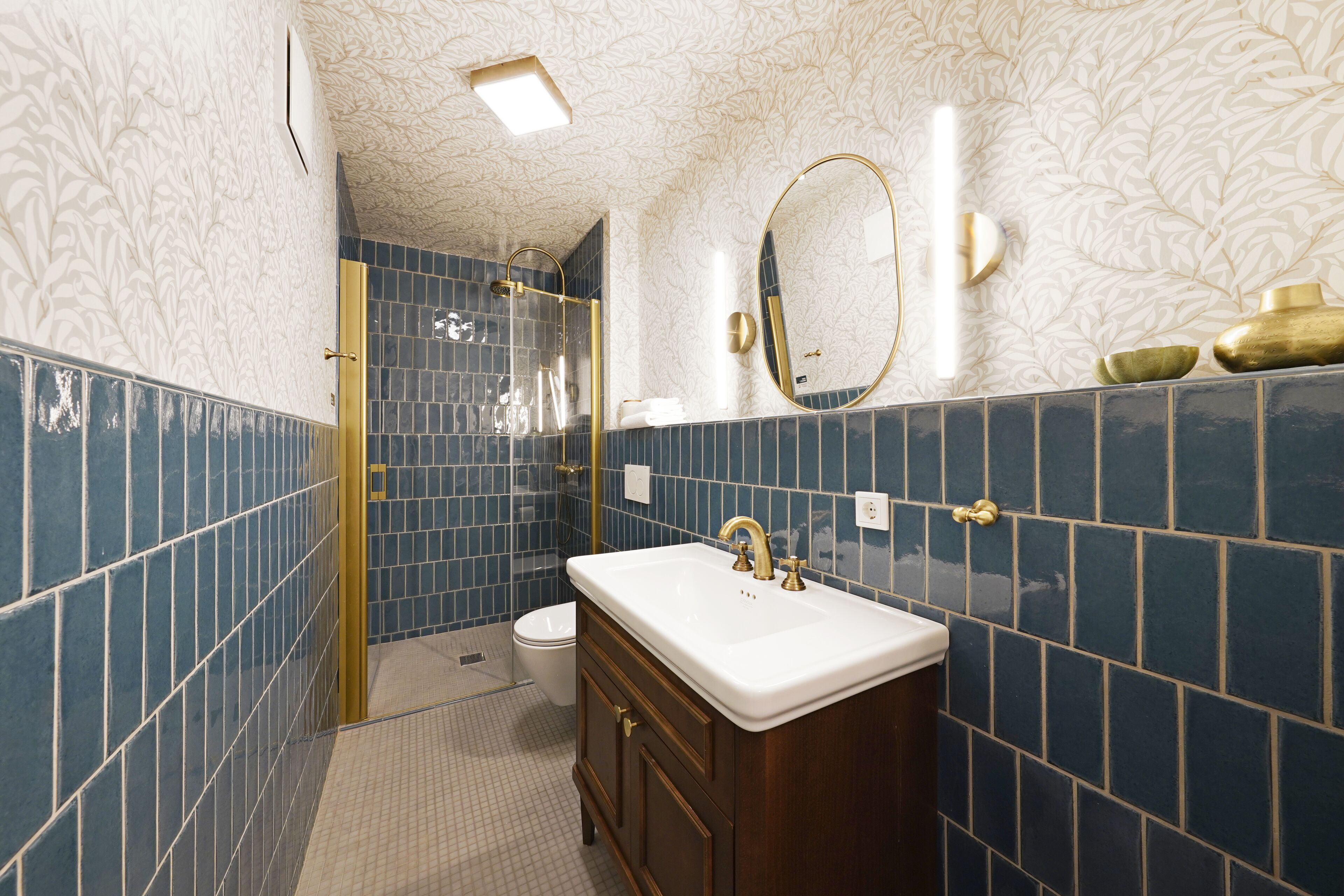 Un baño con un lavamanos blanco, detalles dorados y azulejos azules.