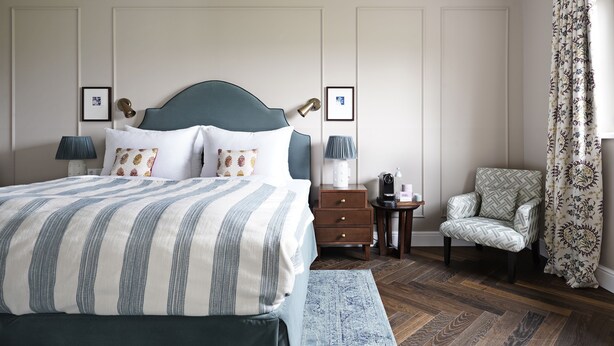 A neatly arranged bedroom with a large bed, bedside tables, a chair, and a patterned curtain. - Numa Salzburg Ivy (Anif)
