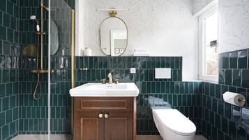Et badeværelse med bruser, håndvask, toilet og spejl.