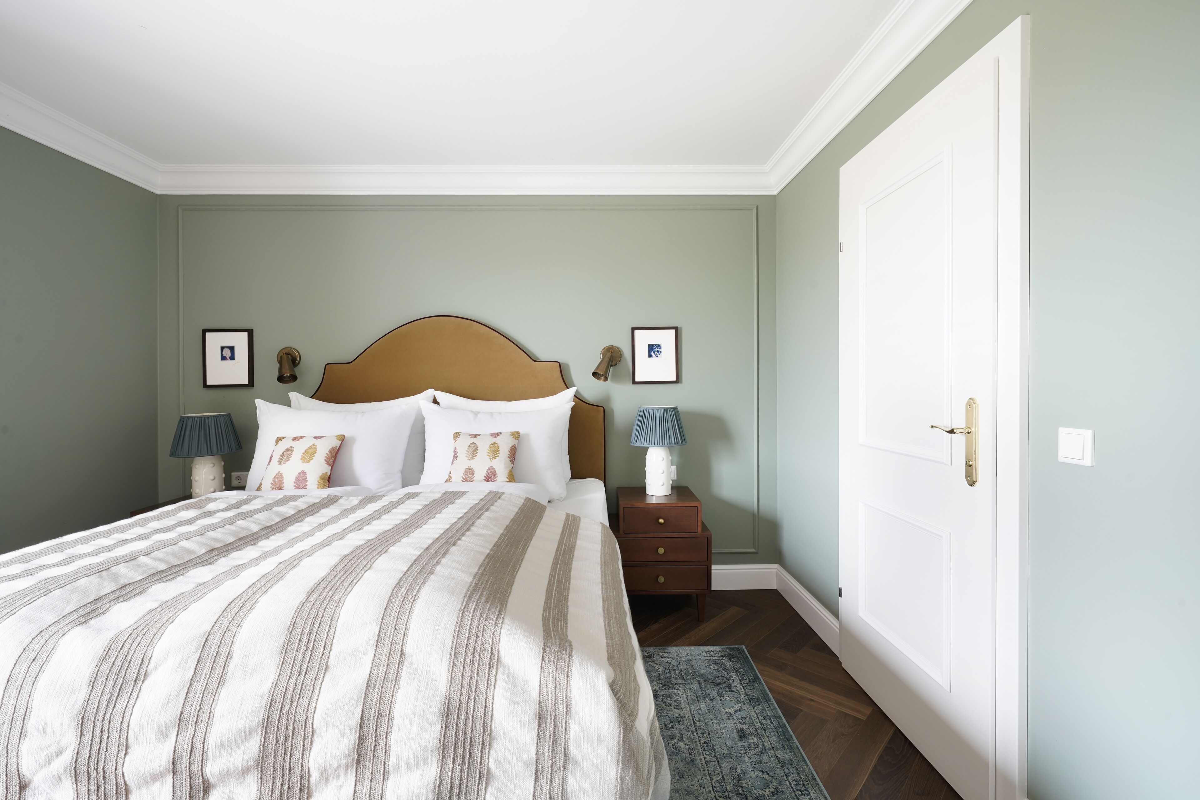 Une chambre à coucher avec un grand lit, deux tables de chevet avec des lampes, une tête de lit en bois et une porte.