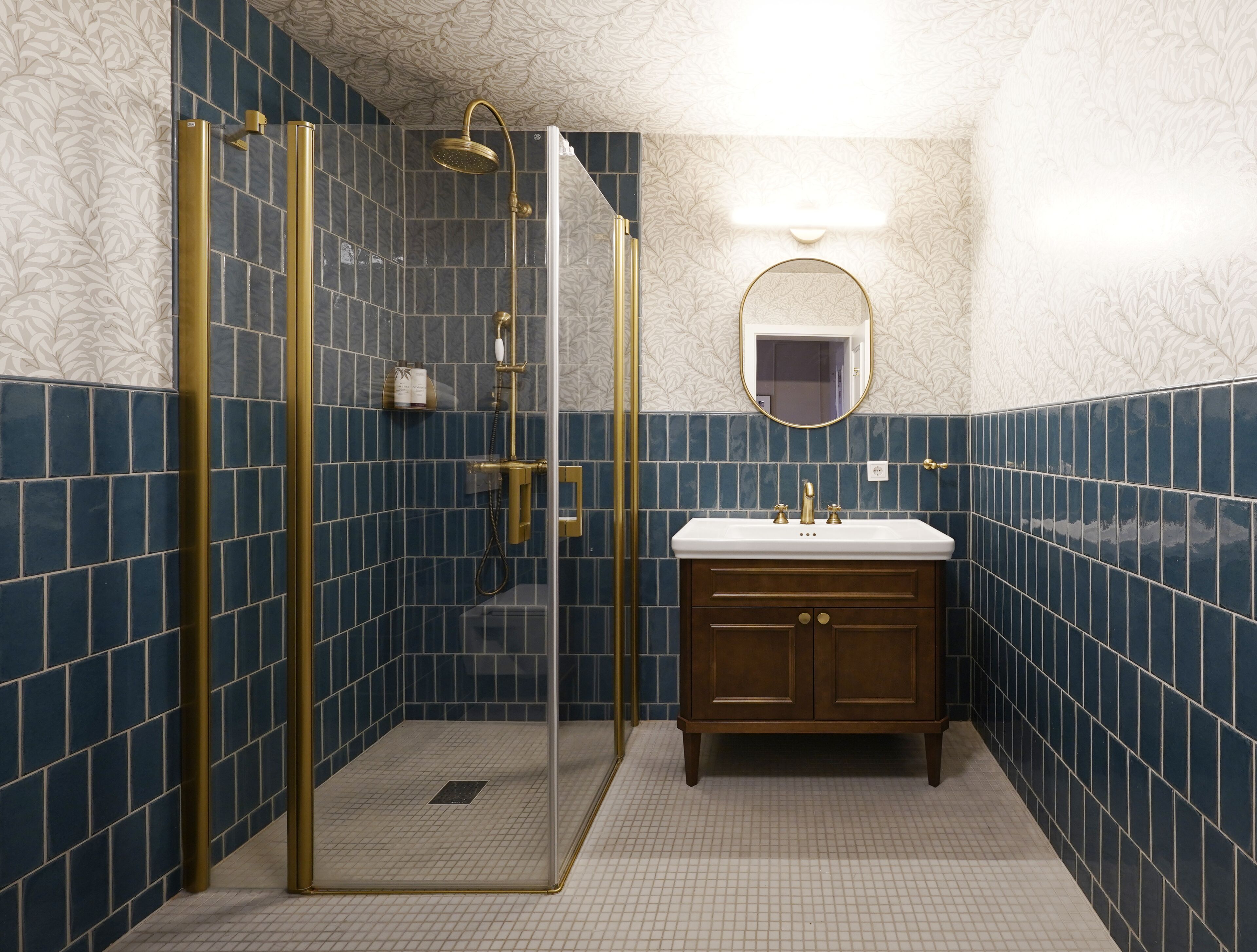 A bathroom with a glass-enclosed shower, a vanity with a mirror, and blue-tiled walls.