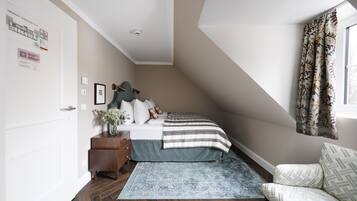 A bedroom with a sloped ceiling, a bed with a striped blanket, a wooden dresser, a vase with flowers, and a patterned rug.