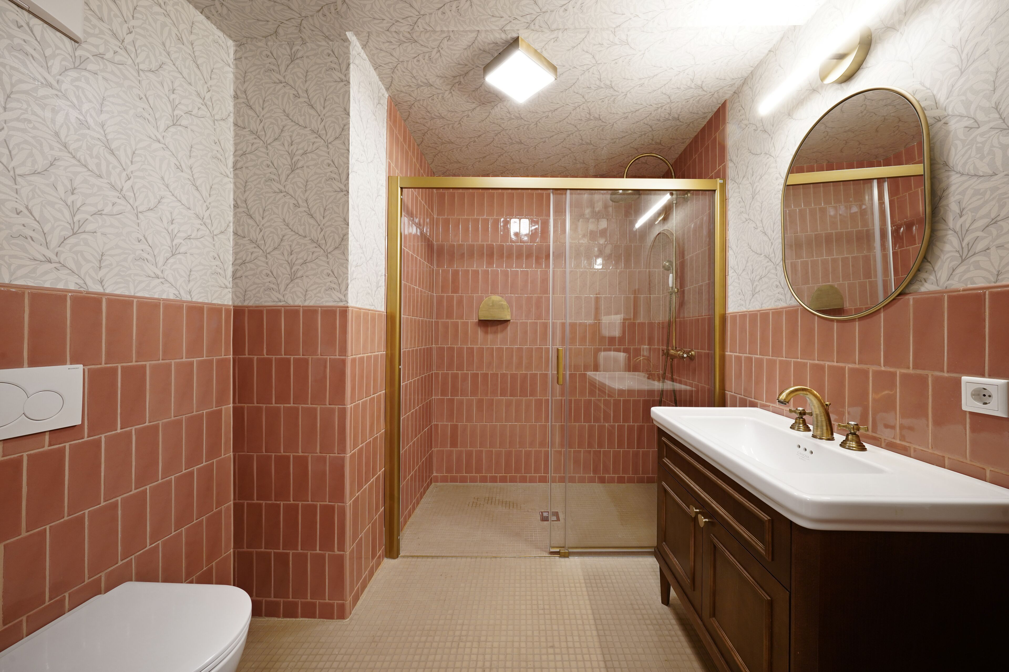 A bathroom with a glass-enclosed shower, a white sink with gold fixtures, and a toilet.