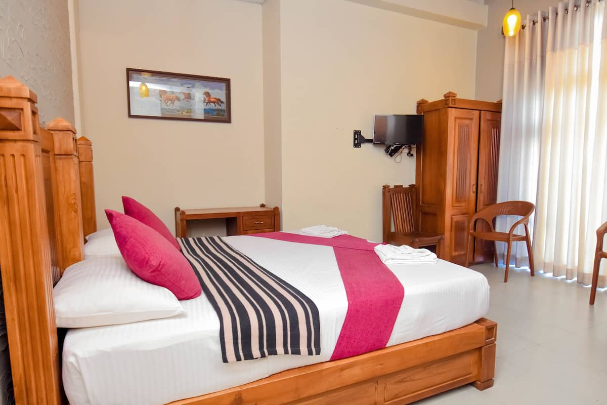 A hotel room with a wooden bed, a desk, a chair, a television, and a wardrobe.