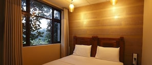 Une chambre à coucher avec une tête de lit en bois, une grande fenêtre avec des rideaux et un luminaire fixé au mur.