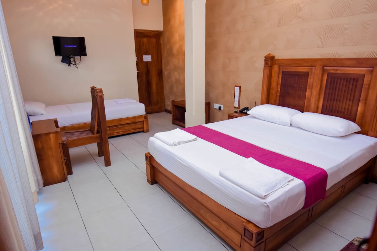 A hotel room with two single beds, a wooden headboard, a flat-screen TV mounted on the wall, and a wooden nightstand.
