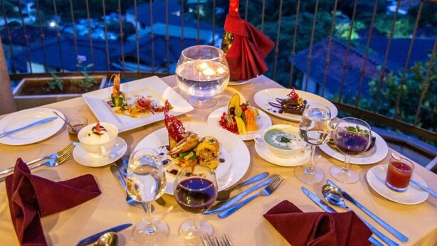 Une table à manger dressée avec des assiettes, des couverts et des verres, offrant une vue panoramique sur une ville au crépuscule.