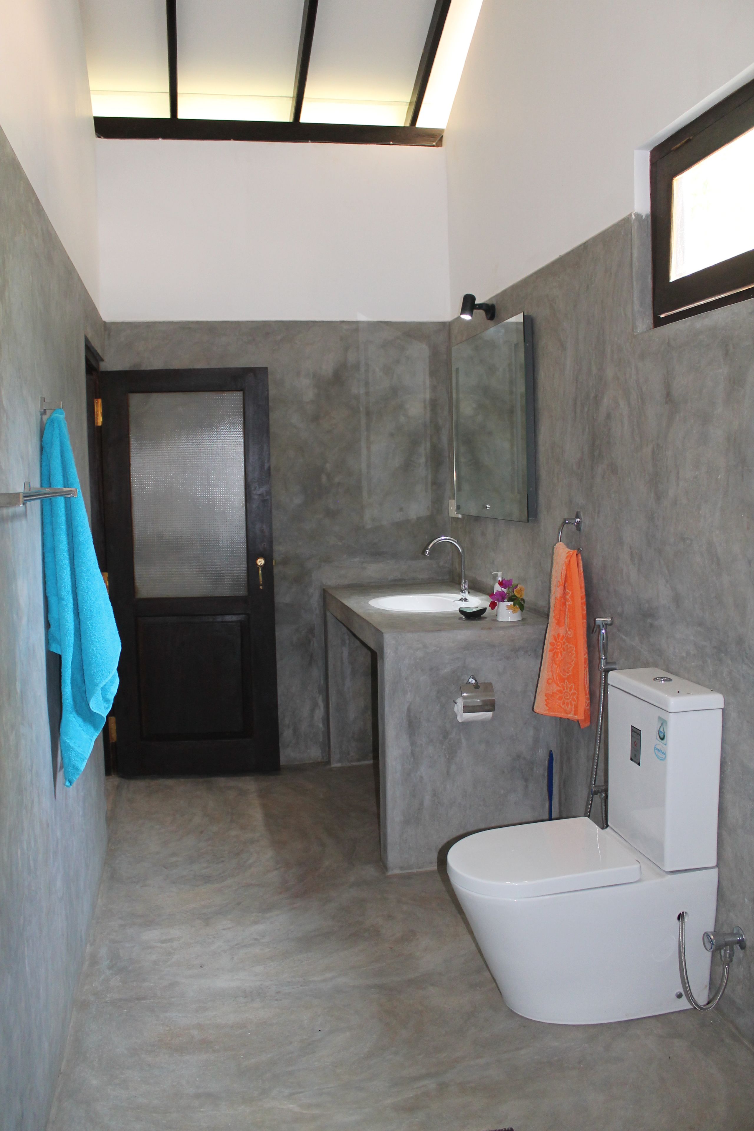 A modern bathroom with a dark door, a white sink, a mirror, and a toilet.